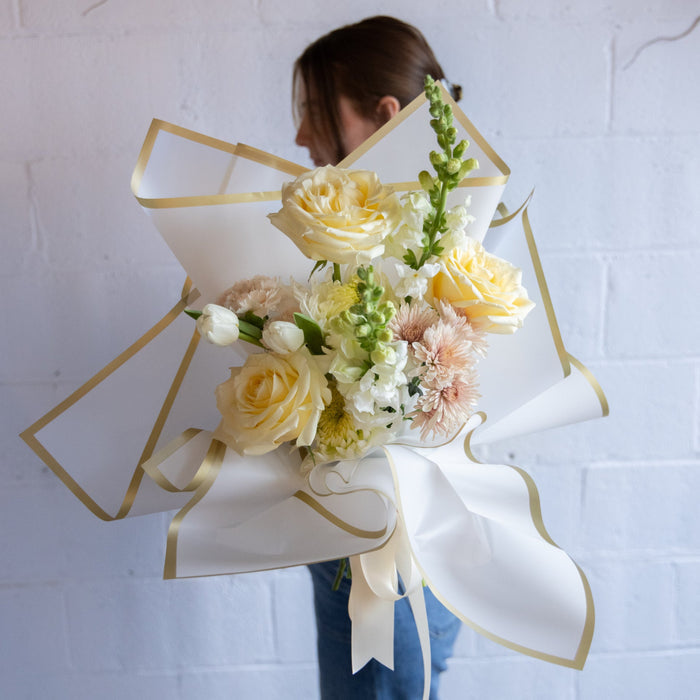 Bouquet of flowers wrapped in white paper with gold ribbons held by a person against a white background